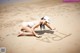 A woman in a white bathing suit and hat writing in the sand.