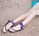 A woman sitting on a beach with her feet in sandals.