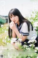 A young woman in a school uniform sitting in a field of flowers.