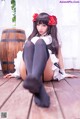 A woman in a maid outfit sitting on a wooden floor.